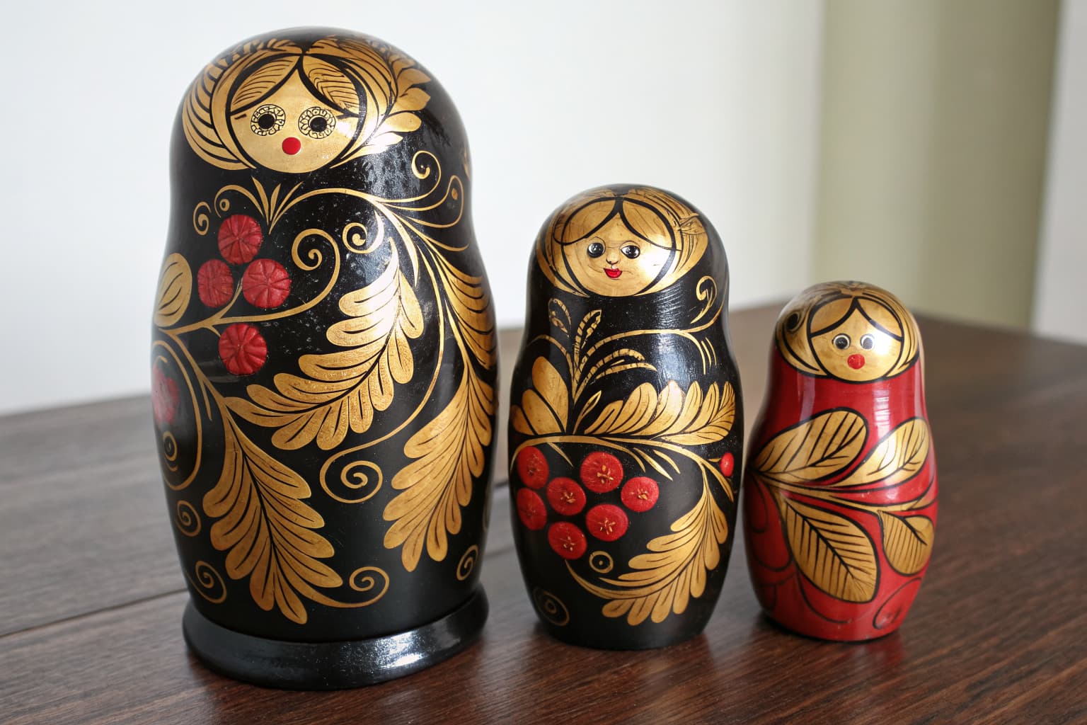 Three Khokhloma lacquered nesting dolls with golden scrollwork